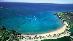 An aerial view of a coastal area with a clear blue sea, a sandy beach, and dense greenery along the shore. - Waikoloa Beach Villas J32 (Waikoloa)
