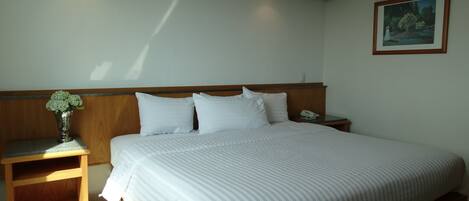 A hotel room with a large bed, wooden headboard, bedside tables, a vase of flowers, and a framed picture on the wall.