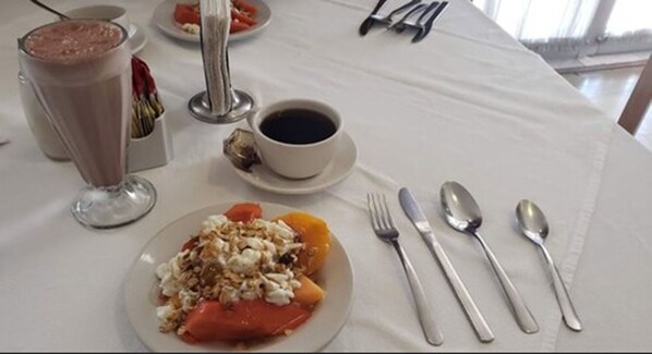Un desayuno con un plato de cereal y fruta, una taza de café y un vaso de leche.