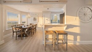 Un vaste espace dédié à la salle à manger, avec une table et des chaises en bois, un luminaire suspendu et une grande horloge murale.