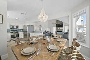 Een moderne keuken met witte kasten, roestvrijstalen apparatuur en een eethoek met een houten tafel voor vier personen.