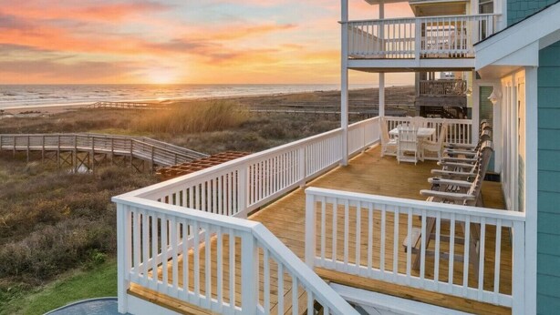 Une propriété située en bord de mer, dotée d’une terrasse en bois, de rampes blanches et d’un espace salon extérieur.