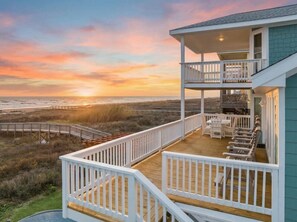 A beachfront property with a wooden deck, white railings, and outdoor seating. - Oceanfront Home with Pool & Private Beach Walkover (Galveston)