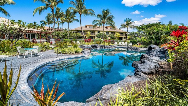 A pool surrounded by tropical plants and palm trees, with a building in the background. - Waikoloa Beach Villas C3 (Waikoloa)