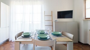 A dining area with a table set for four, including plates, glasses, and cutlery. There is a TV mounted on the wall above the table. - Il Borgo apartments - B5 (Finale Ligure)