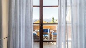 An open door leading to a balcony with a table and chairs, a view of mountains, and a clear sky. - Il Borgo apartments - B5 (Finale Ligure)