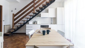 A modern kitchen with white cabinets, a wooden staircase, and a dining area with a table and chairs. - Il Borgo apartments - B5 (Finale Ligure)