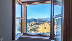 A window with a view of a hillside village, buildings, and mountains. - Il Borgo apartments - B5 (Finale Ligure)