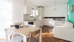 A compact kitchen with white cabinets, a dining table with chairs, and a small sofa. - Il Borgo apartments - B6 (Finale Ligure)