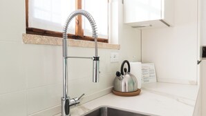 A modern kitchen with a stainless steel sink, a flexible faucet, a kettle on the counter, and a window above the sink. - Il Borgo apartments - B6 (Finale Ligure)