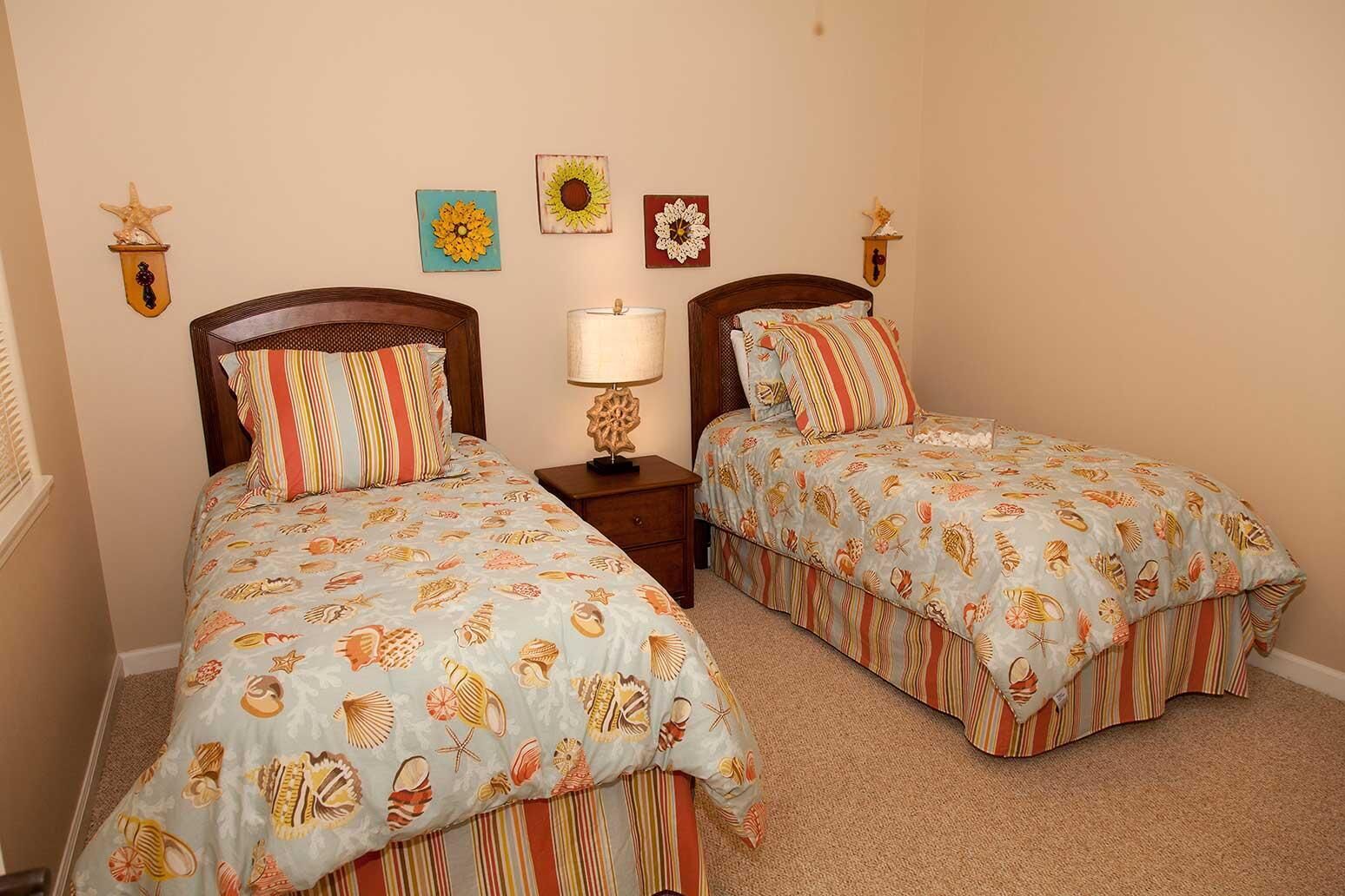 Un dormitorio con dos camas individuales, cada una con ropa de cama a rayas y una decoración con forma de estrella de mar. Hay una mesita de noche con una lámpara entre las camas.