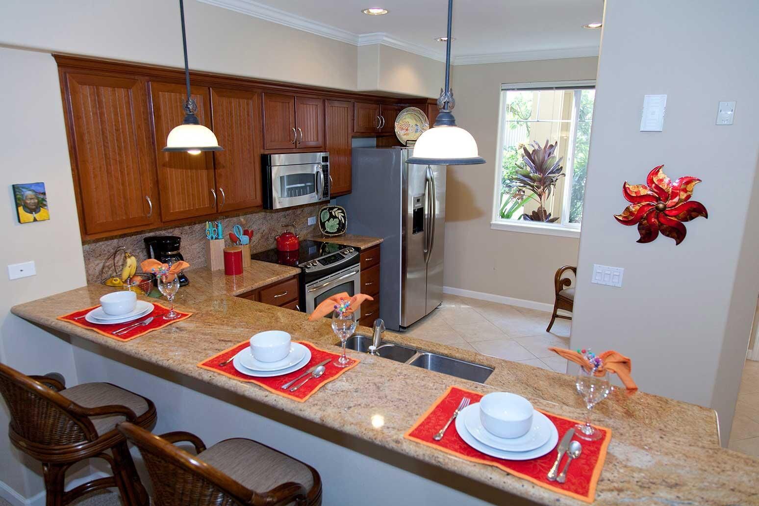 A modern kitchen with granite countertops, wooden cabinets, stainless steel appliances, and a breakfast bar with red placemats.