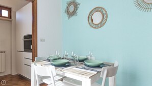 A dining area with a table set for four, white chairs, and two wall decorations. - Il Borgo apartments - C3 (Finale Ligure)