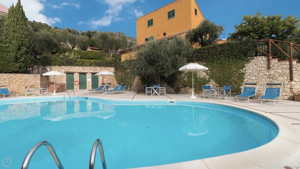 A swimming pool with lounge chairs and umbrellas, surrounded by stone walls and greenery. - Il Borgo apartments - C3 (Finale Ligure)