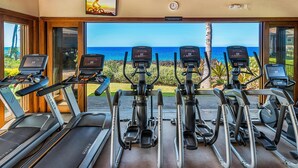 A fitness center with treadmills and elliptical machines, large windows with a view of the ocean, and a wooden ceiling. - Halii Kai at Waikoloa 2B (Waikoloa)