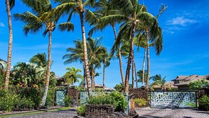 A tropical resort entrance with palm trees, a paved driveway, and a gated entrance. - Halii Kai at Waikoloa 2B (Waikoloa)