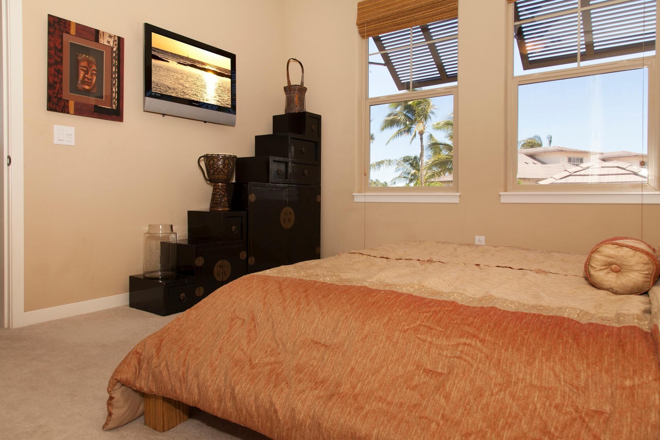 Une chambre à coucher avec un lit, une commode, un téléviseur et une fenêtre donnant sur des palmiers.