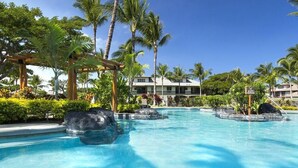 A pool area with clear blue water, palm trees, and a building in the background. - Golf Villas at Mauna Lani - Unit K5 (Kamuela)