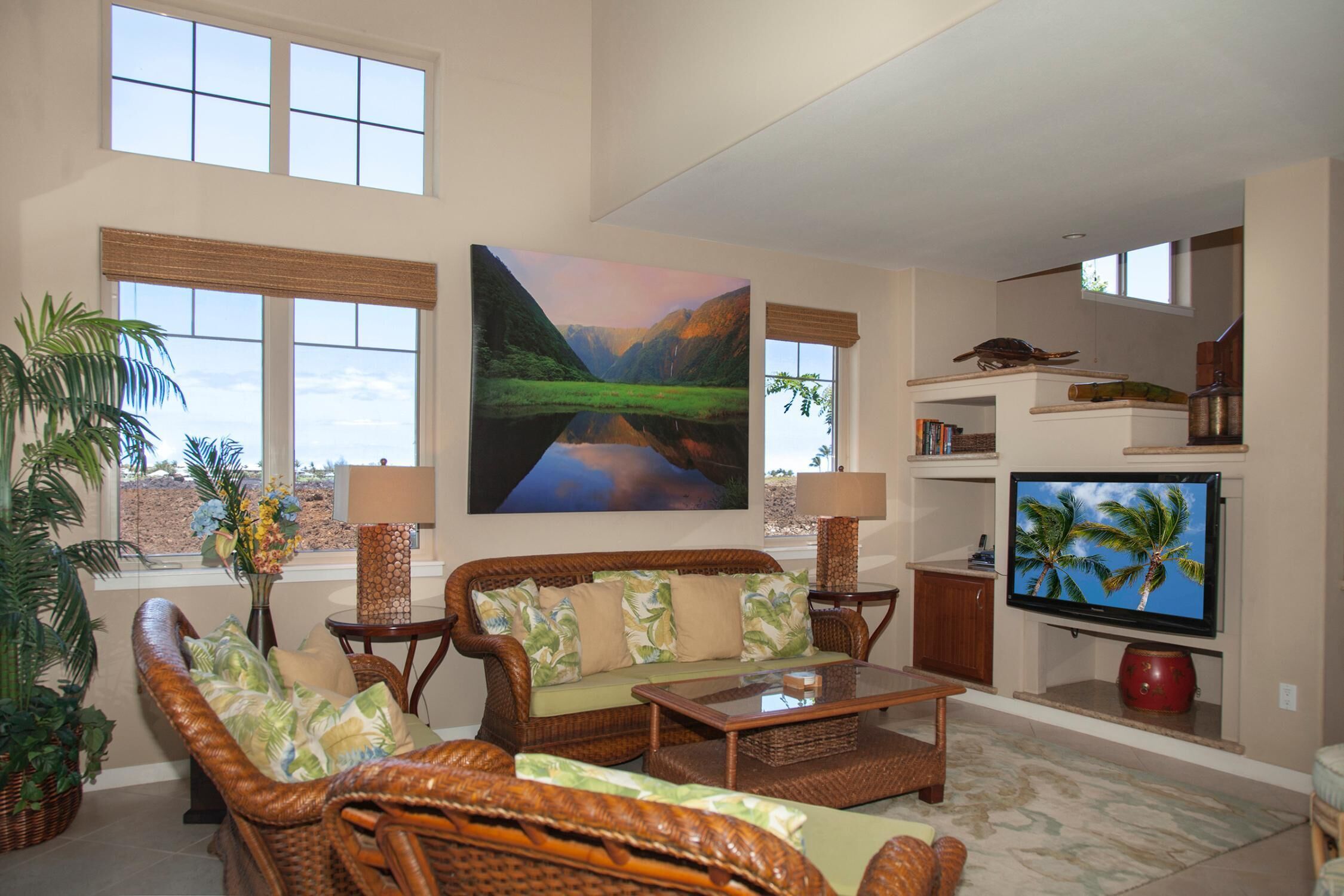 A spacious living room with a large window, a wicker sofa, a flat-screen TV, and a bookshelf.