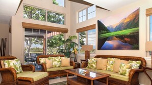 A spacious living room with wicker furniture, large windows, and a painting of a landscape. - Golf Villas at Mauna Lani - Unit K5 (Kamuela)