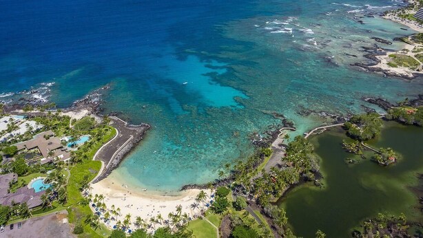 An aerial view of a coastal resort with clear turquoise waters, a sandy beach, and lush greenery. - Golf Villas at Mauna Lani - Unit K5 (Kamuela)