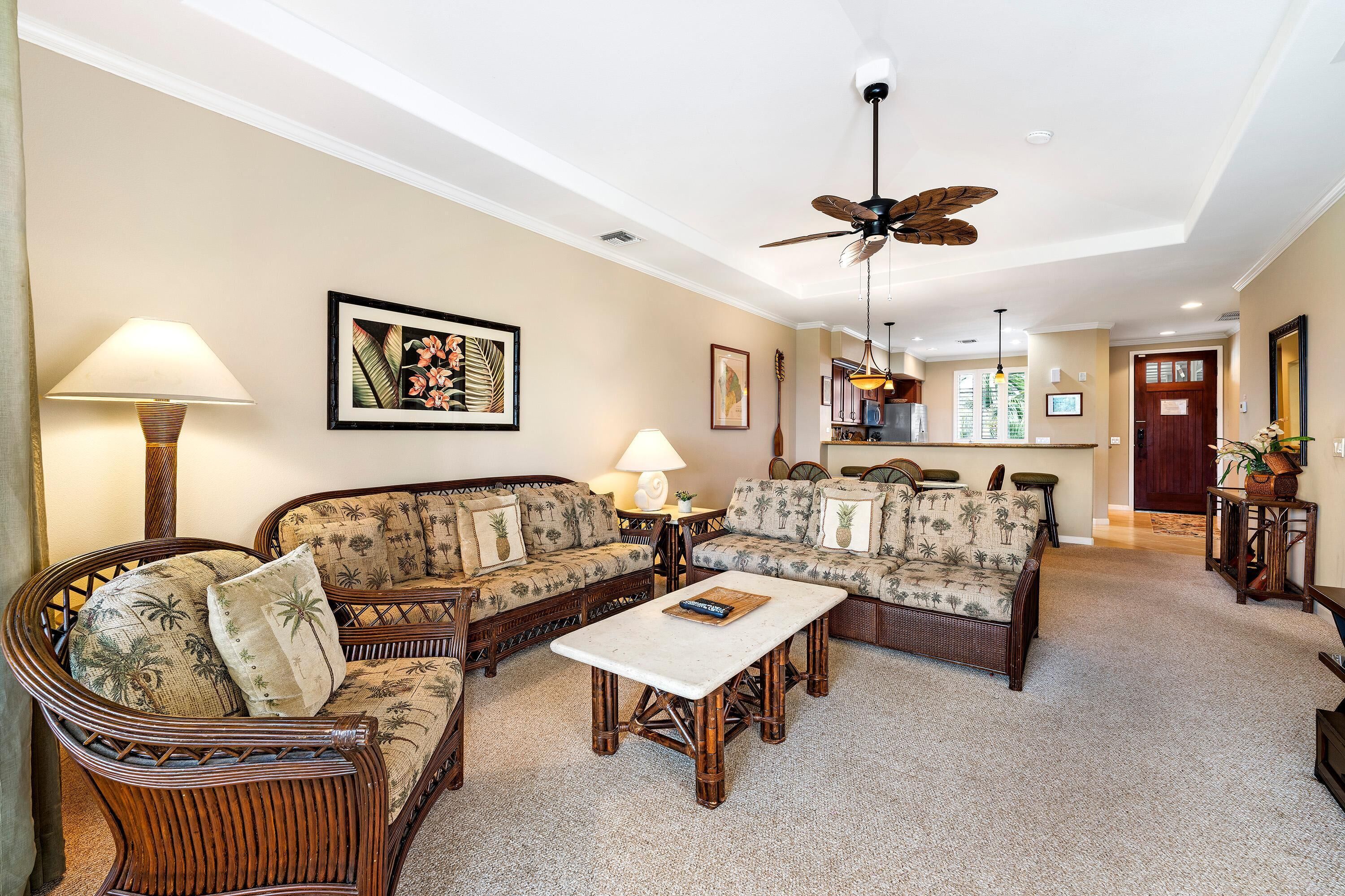 A spacious living room with a rattan sofa set, a coffee table, and a ceiling fan.