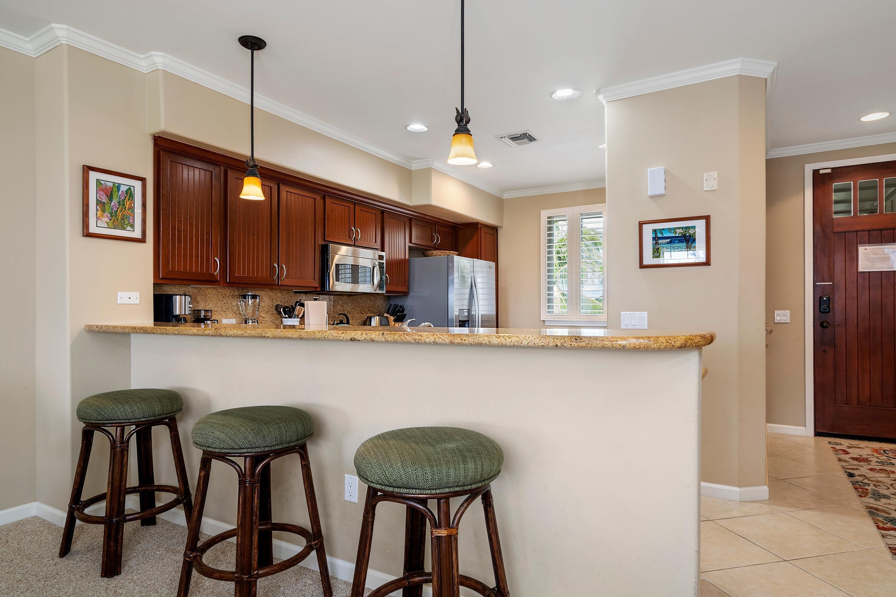 A kitchen with wooden cabinets, a granite countertop, and three green barstools.