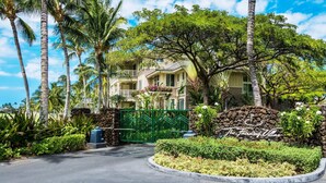 A gated entrance to a multi-story building with a landscaped garden and palm trees. - Fairway Villas Waikoloa A21 (Waikoloa)