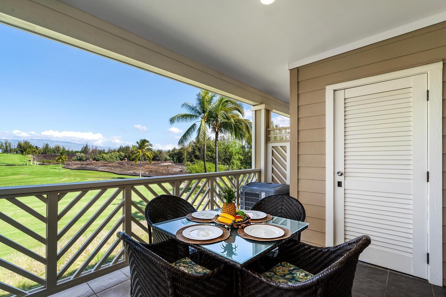 A balcony with a table set for four, overlooking a golf course with palm trees.