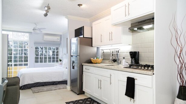 Una cocina compacta con armarios blancos, un refrigerador, una estufa y una cafetera.