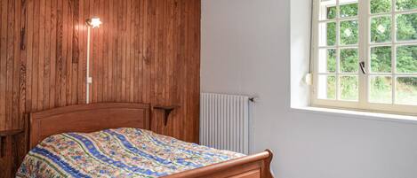 Un dormitorio con cabecera de madera, un radiador y una ventana con vista a la vegetación.