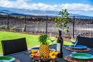 A table set outdoors with a bottle of wine, glasses, plates, and a fruit basket.