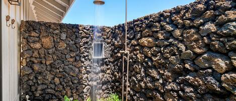A stone wall with a built-in showerhead, a wooden deck, and potted plants.