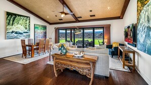 A spacious living room with a dining area, large windows, and a ceiling fan.
