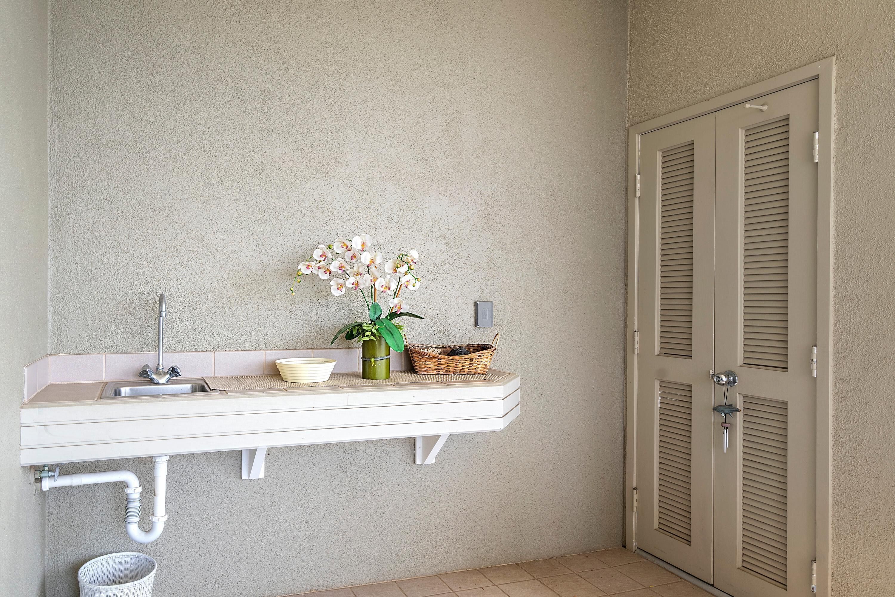 A bathroom with a white sink, a mirror, a potted orchid, and a wicker basket.