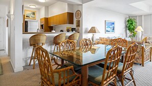A modern kitchen with wooden cabinets, a glass dining table, and wicker chairs. - Vista Waikoloa B206 (Waikoloa)