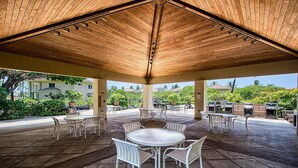 A covered patio area with a round table and chairs, outdoor kitchen, and potted plants. - Vista Waikoloa B206 (Waikoloa)