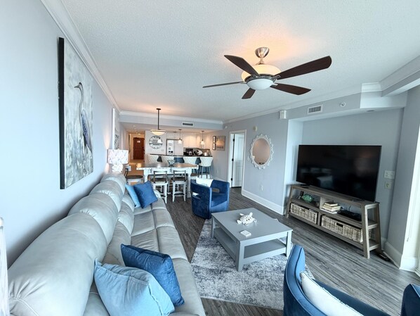 A living room with a sofa, coffee table, TV, and a ceiling fan. - Gorgeous 3br/3ba Ocean view Southern side unit (North Myrtle Beach)