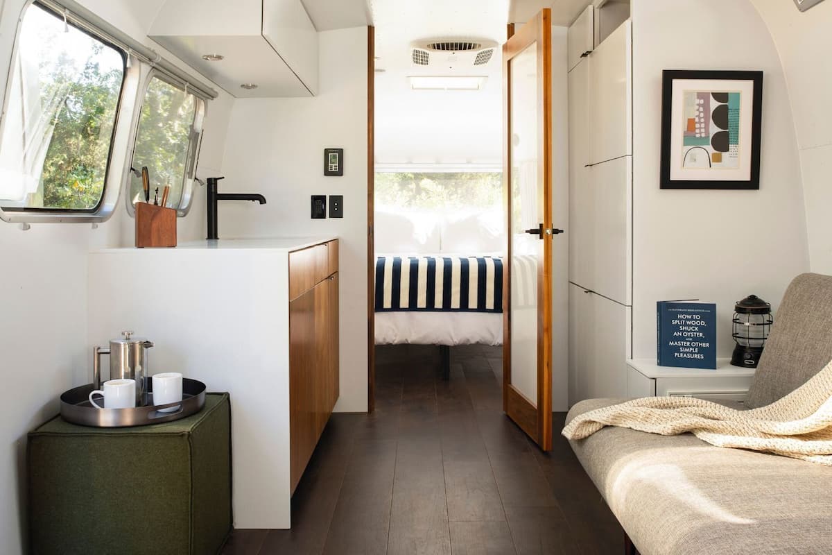 Interior compacto de una caravana con kitchenette, cama, zona de estar y ventana con vistas al exterior.