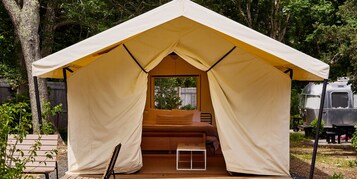 A tent with a bed inside, surrounded by trees and a parked camper.