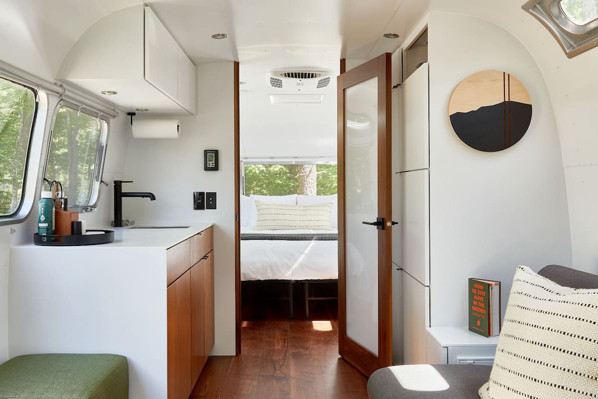 Interior compacto de una autocaravana con kitchenette, cama y una pequeña zona de estar.