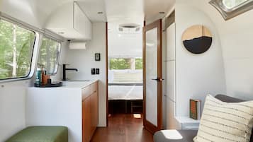 A compact RV interior with a kitchenette, a bed, and a small seating area.