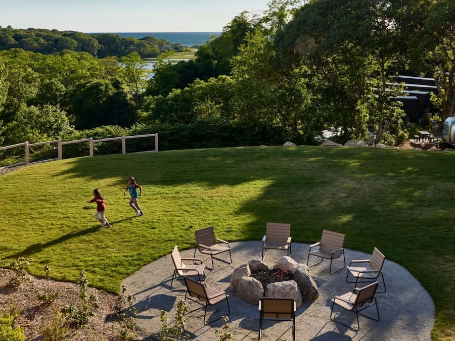 A backyard with a fire pit and outdoor seating, surrounded by trees and a view of the ocean.