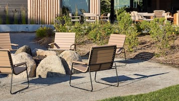 An outdoor seating area with chairs and tables, surrounded by rocks and plants.