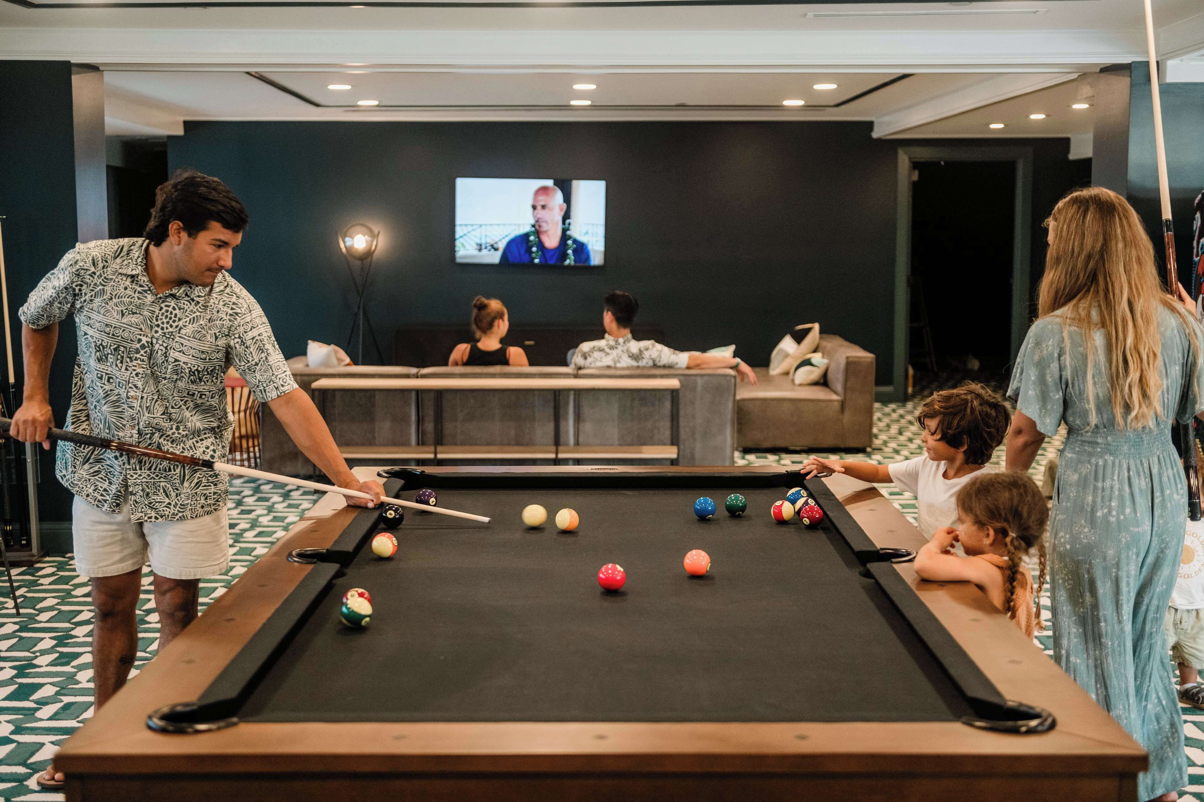 Une table de billard dans une pièce où l’on aperçoit un écran de télévision au fond.