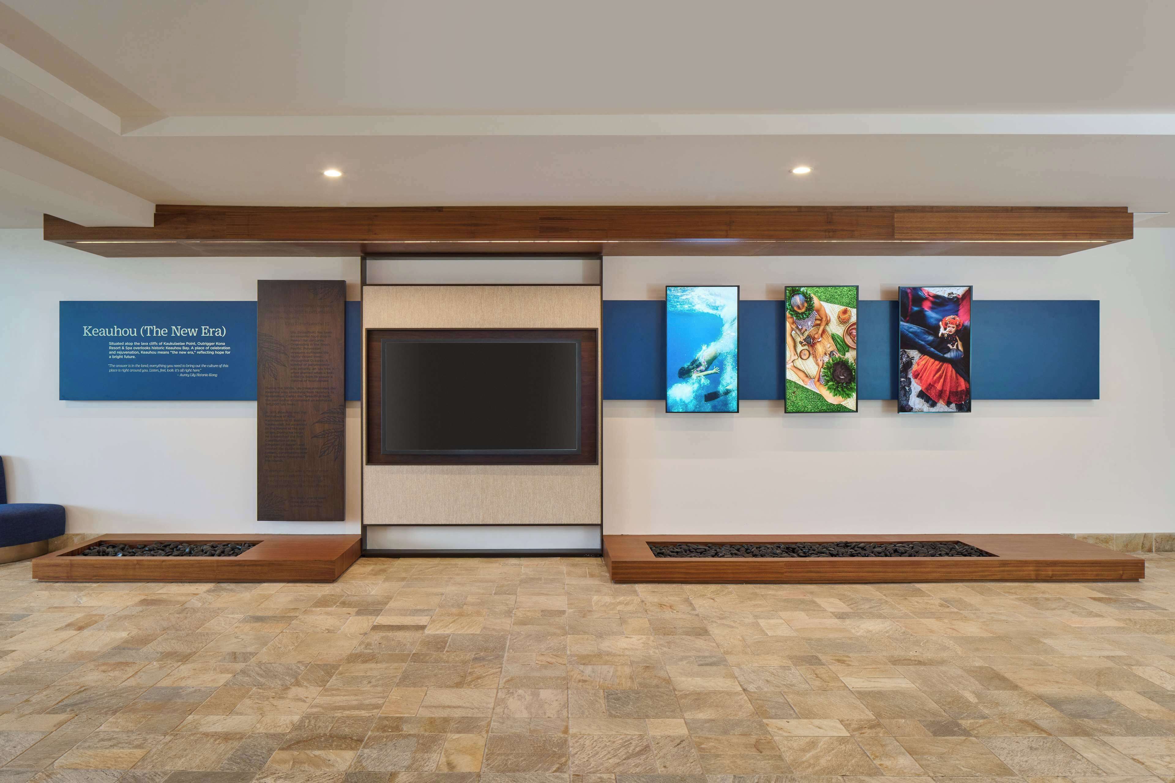 A modern lobby with a large flat-screen TV, a wooden bench, and three framed artworks on the wall.
