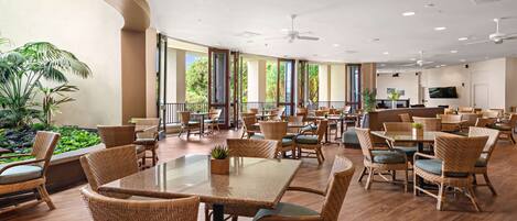 A spacious indoor dining area with wicker furniture, large windows, and a flat-screen TV.
