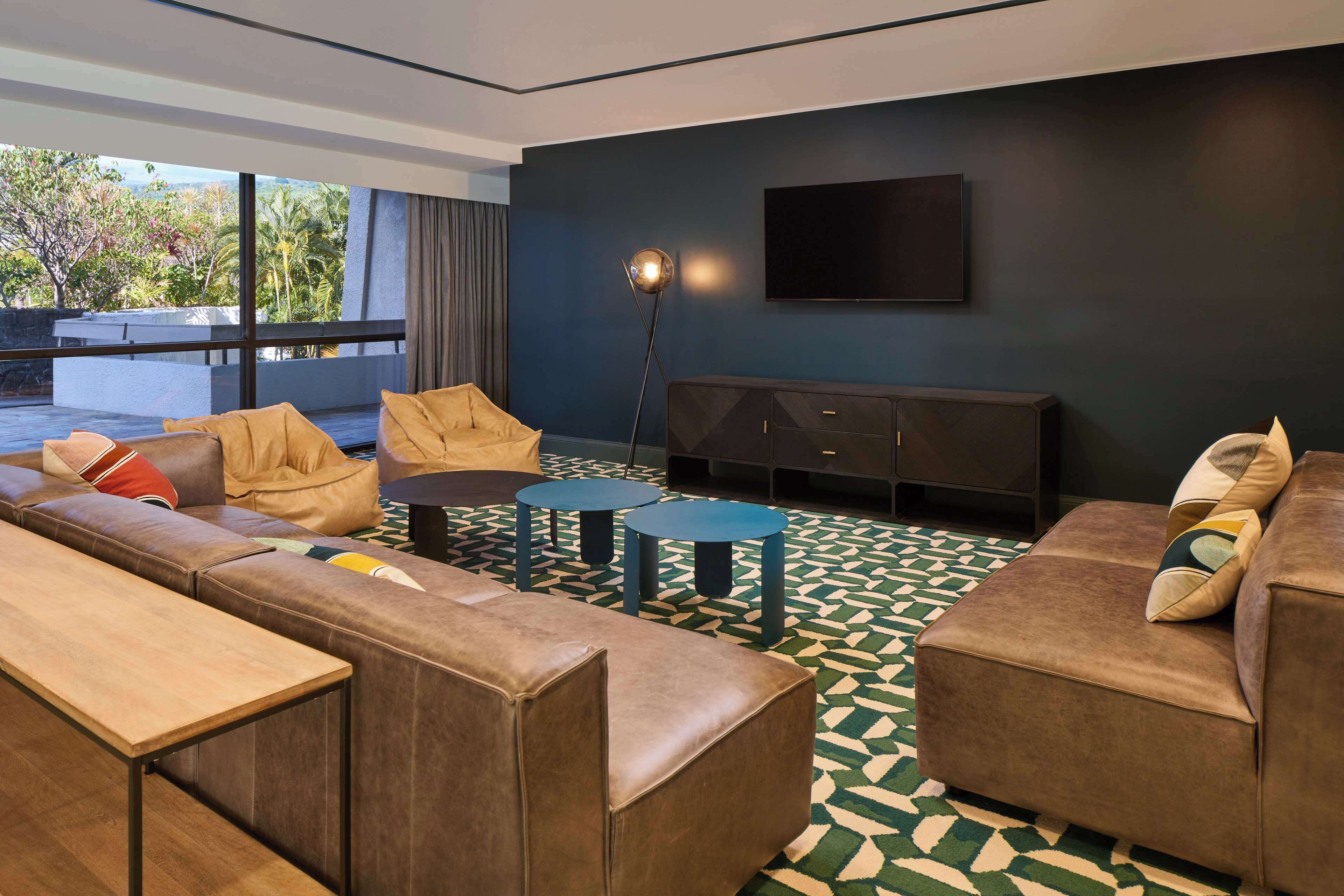A modern living room with a sofa set, two round tables, a TV mounted on the wall, and a patterned floor.