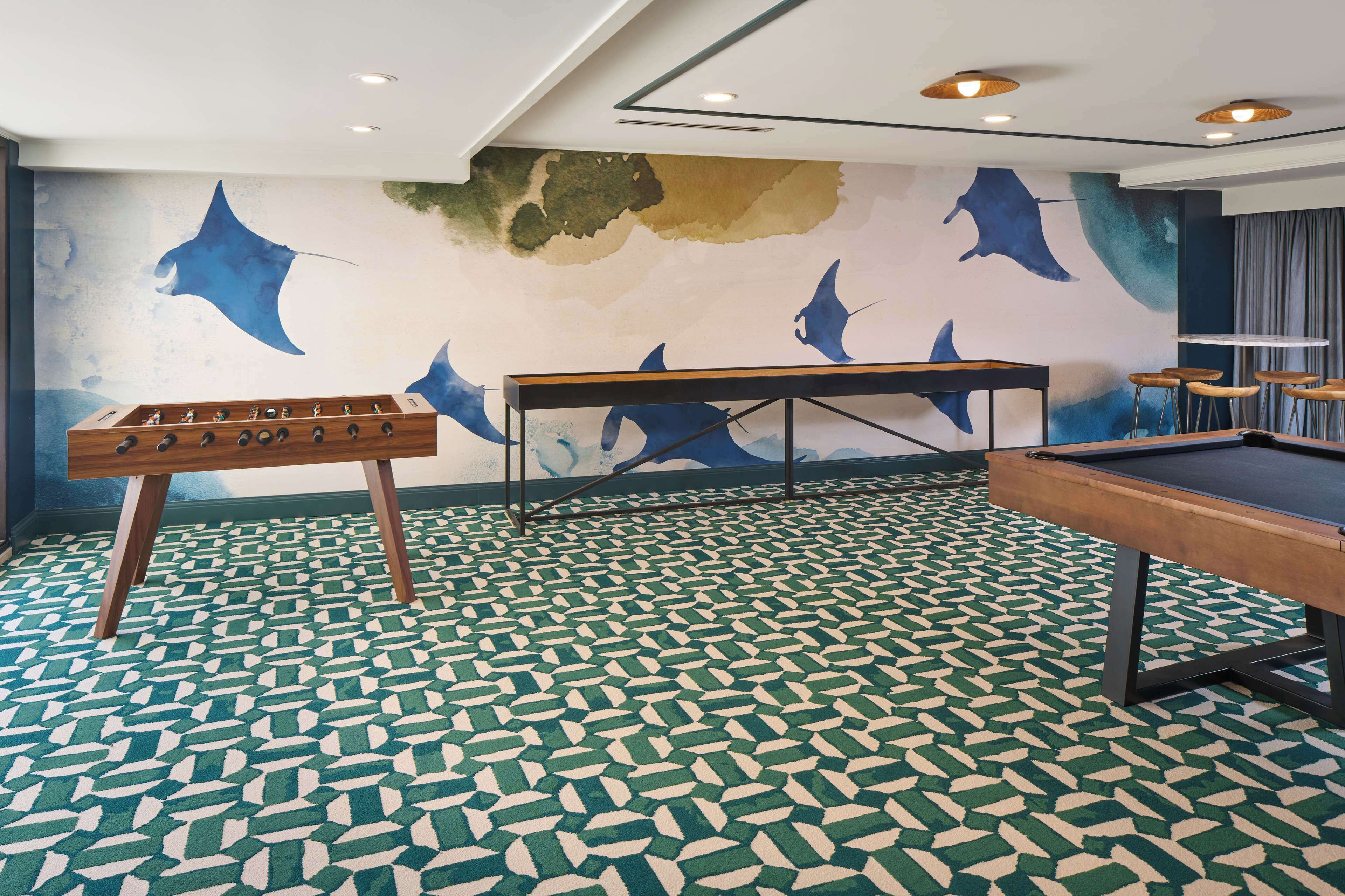 Una habitación con mesa de fútbol de mesa, mesa de billar y un mural en la pared con peces azules.