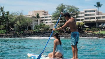 A man and a woman on a paddleboard in a coastal area with buildings in the background.